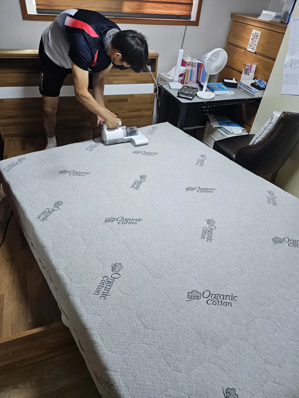 몸을 숙여 윗면을 침구청소기로 훑는 모습 — 매트리스 황변 제거 2단계