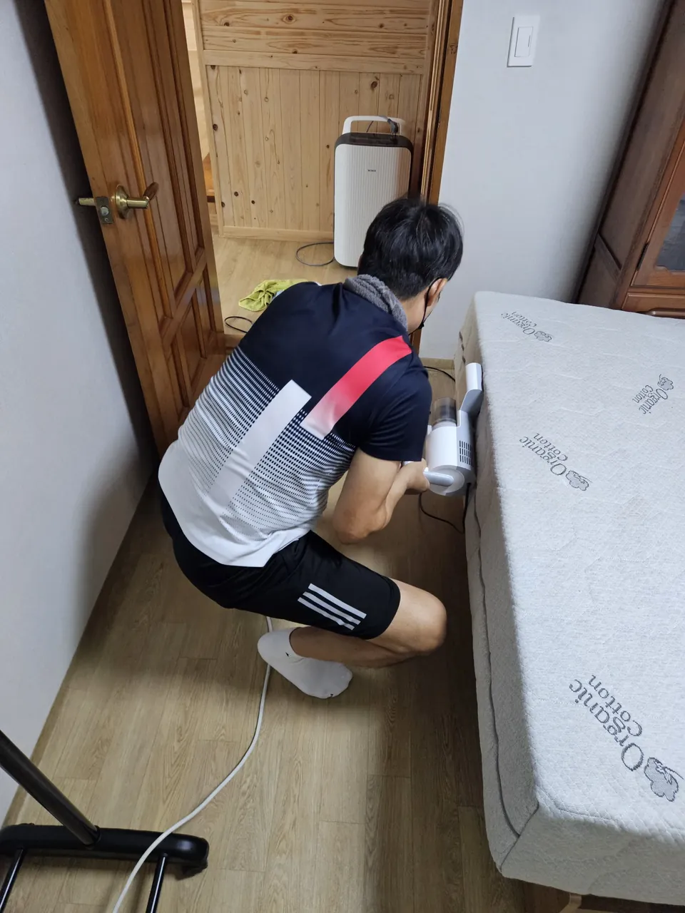 쪼그려 앉아 매트리스 옆면 모서리를 흡입하는 모습 — 매트리스 모서리 청소 2단계